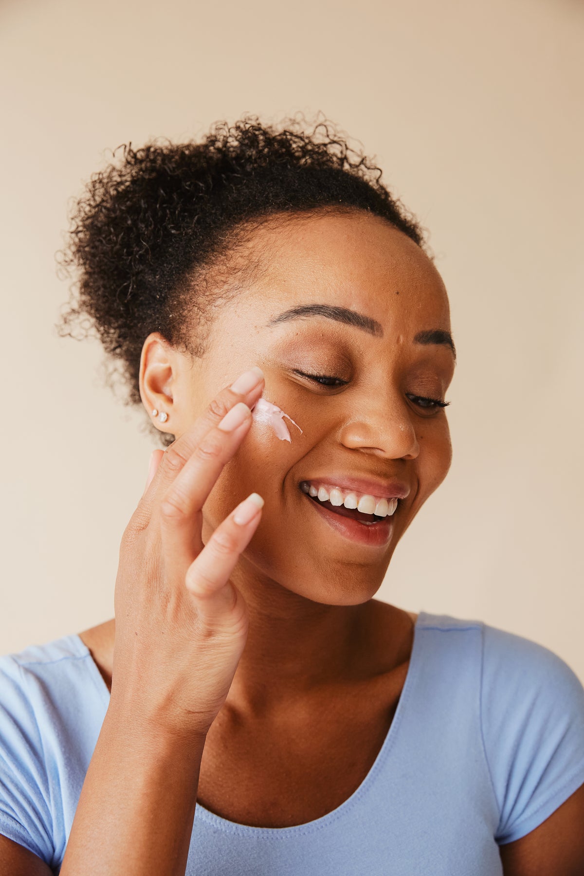Person applying face cream with fingertips against a neutral beige background.